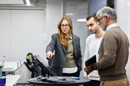 A group of professionals engaging in a discussion while examining a digital screen in a modern office environment.
