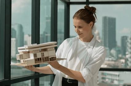 A woman holding a scale model of a modern building in a bright office space.