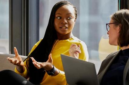 Two women engaged in a conversation in a modern office setting.
