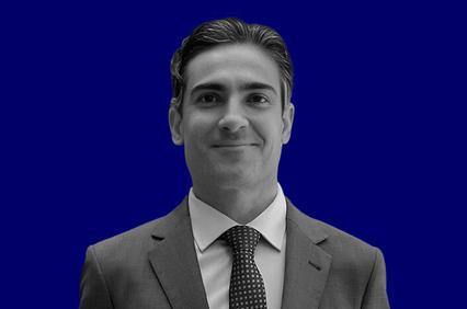 A grayscale image of a smiling young man in a suit, set against a solid blue background.