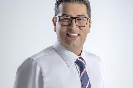 A smiling man in a white shirt and striped tie poses against a light background.