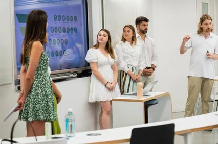 A group of four young professionals is presenting in front of a screen displaying data charts.