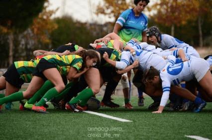 A women's rugby match showing two teams engaged in a scrum on a grass field.