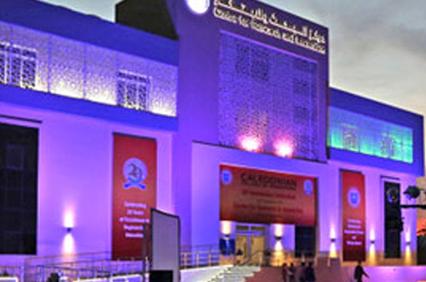 Illuminated building at night with Arabic inscriptions and people walking outside.