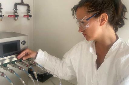 A woman in protective gear is operating a laboratory device with multiple tubes.
