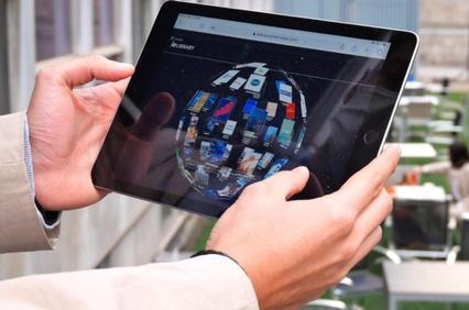 A person holding a tablet displaying a colorful digital model of a building in an office environment.