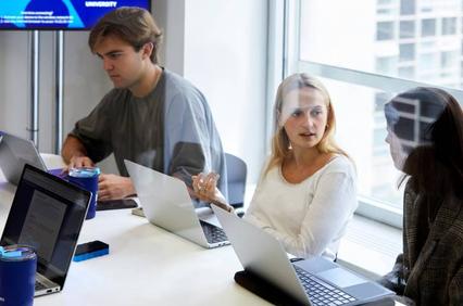 Three people, two women and one man, are working on laptops in a modern office environment.