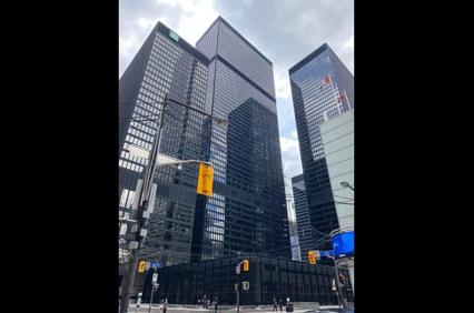 A view of modern, dark glass skyscrapers with street traffic lights in the foreground under a cloudy sky.
