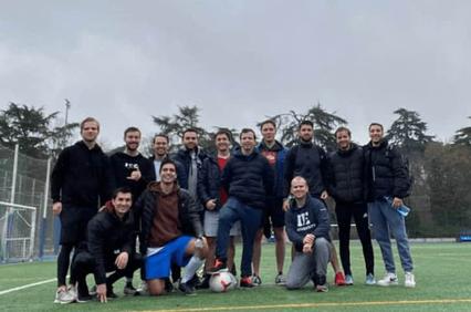 A group of men posing on a soccer field, mostly standing with two kneeling in front.