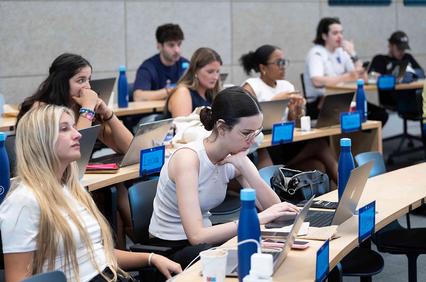 A group of students attentively working on laptops in a classroom setting.