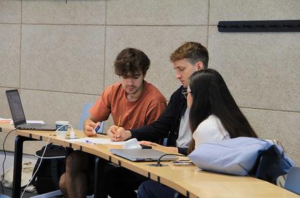 A group of students collaborating on a project at a table with a laptop and notes.