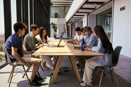 A group of young professionals engaged in a meeting around a large table in a modern office.