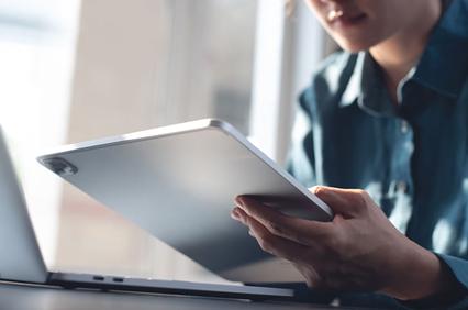 A person is holding a tablet while sitting at a desk with a laptop.