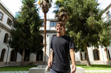 A young man smiling in a courtyard surrounded by palm trees and historic buildings.