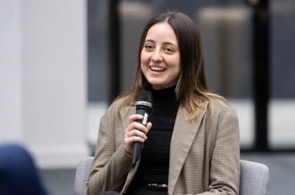A woman smiles while holding a microphone in a discussion panel setting.
