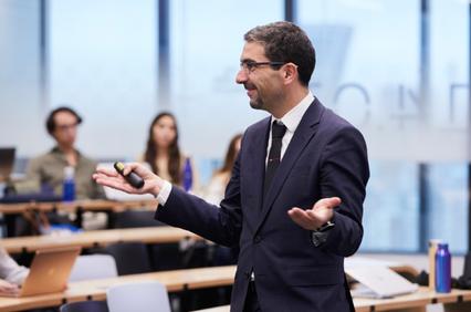 A man in a suit gives a presentation to an audience in a classroom setting.