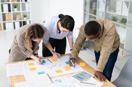Three people collaborating on a project at a table with notes and documents.