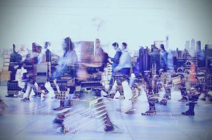 Blurred image of busy people moving in a cityscape environment, suggesting motion and urban life.