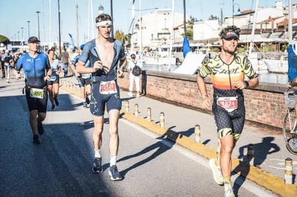 Three men participating in a triathlon running beside a marina.