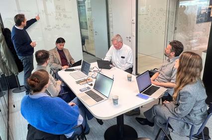 A group of professionals engaged in a collaborative meeting around a conference table with a presentation in progress.