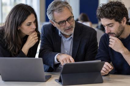 A group of three professionals collaboratively discussing over a tablet in a modern office environment.