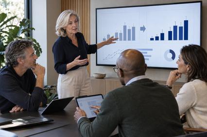 A woman presents a growth chart during a business meeting with three colleagues.