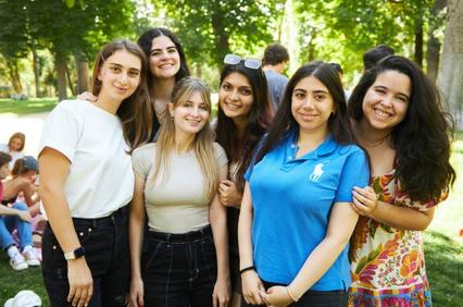 A group of six young women smiling together in a sunny park.