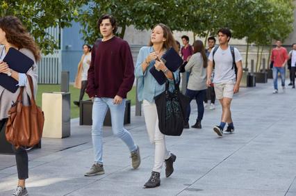 Young adults walking in an urban outdoor plaza, looking casual and busy.
