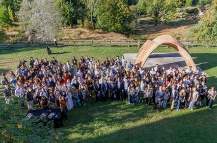A large group of people gathered outdoors in front of an arch-shaped structure.