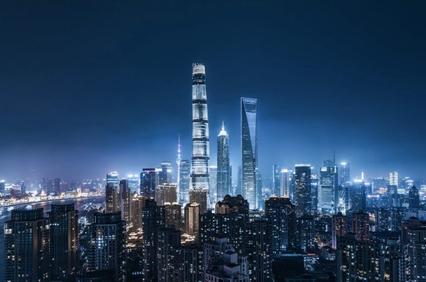 Aerial view of a city skyline at night with illuminated skyscrapers under a dark blue sky.