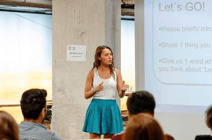 A woman speaking at a workshop in front of a projected presentation slide.