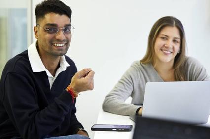 A man and a woman smiling and interacting at a table with a laptop.