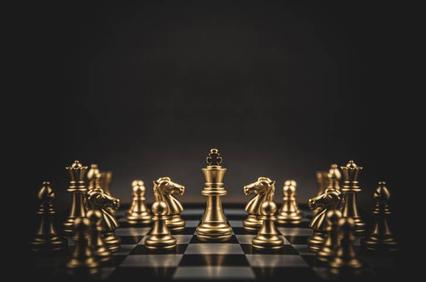 A golden chess set with pieces arranged on a black and white board under dramatic lighting.