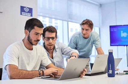 Three young men collaborating on a laptop in a modern office setting.