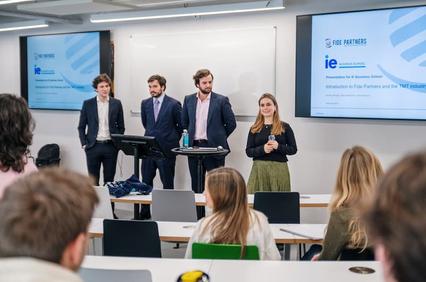 A group of four presenters stands in front of an audience during a business seminar.
