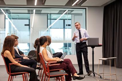 A presenter is giving a speech to an attentive audience in a modern conference room.