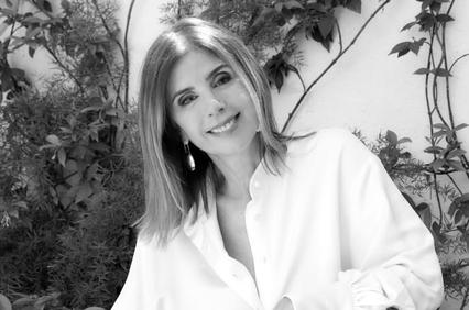 A black and white photo of a smiling woman in a white shirt standing against a background of green foliage.