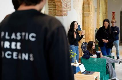 A group of people in an informal meeting space, one wearing a jacket with 'Plastic Free Oceans' written on the back.