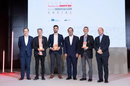 Six men standing on stage at an awards ceremony, holding trophies, with a backdrop of a banner about social innovation.