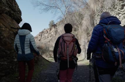 Three people with backpacks walking through a rocky path.