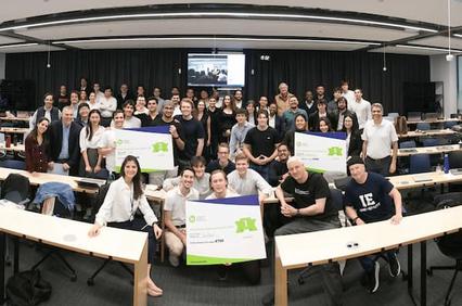 A diverse group of people gathered together in a classroom setting, holding certificates and smiling for a photo.