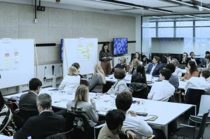 A professional meeting in a modern conference room with a presenter at the front.