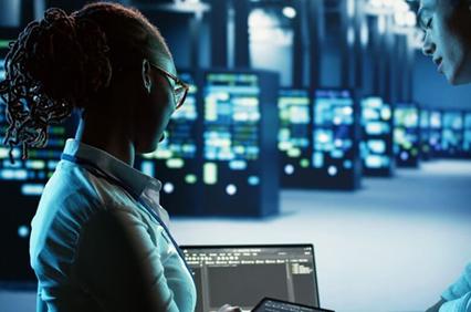 A woman is using a laptop in a data center with servers in the background.