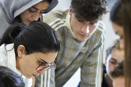 A group of young adults intently looks at something below the frame, possibly focusing on a project or discussion.