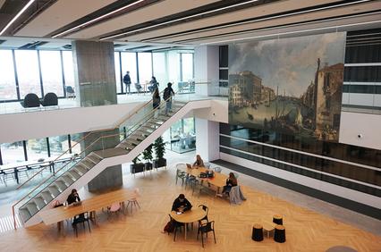 A modern indoor space featuring a large mural, a staircase, and people seated at tables.