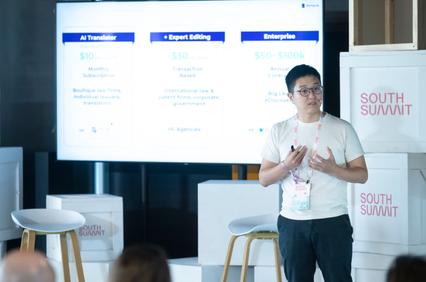 A person presenting at a tech conference with a slide showing service pricing behind them.