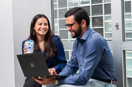Two people are engaged in a friendly conversation while working on a laptop.