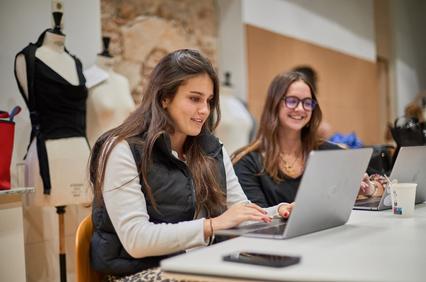 Two women working on laptops in a modern workspace.