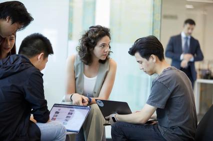 A group of people discussing and working on laptops in a modern office setting.
