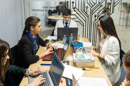 A group of professionals working and discussing at a busy office table with laptops and documents.